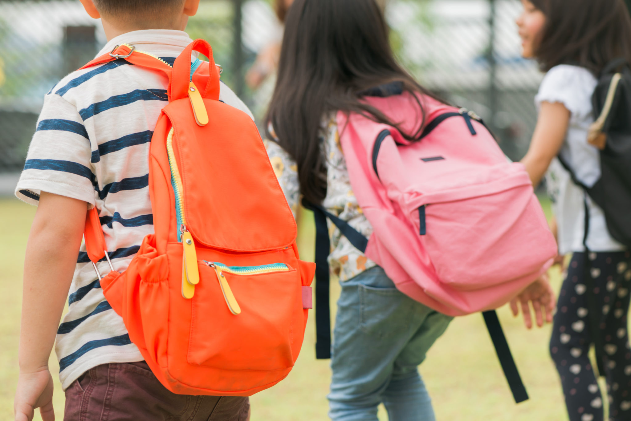 Three children wearing backpacks in the playground