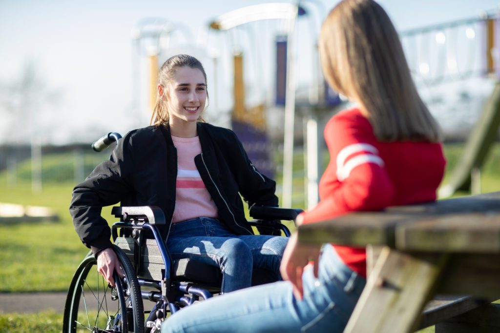 A girl in a wheelchair and a friend sitting outside