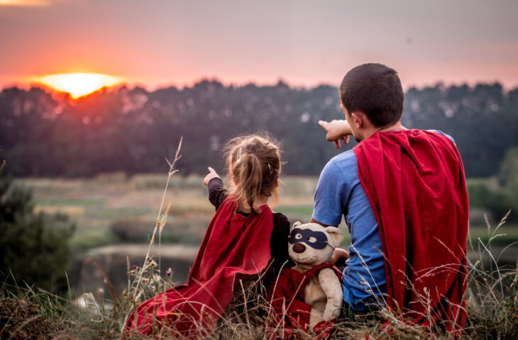 Father and daughter wearing capes pointing at the sunset